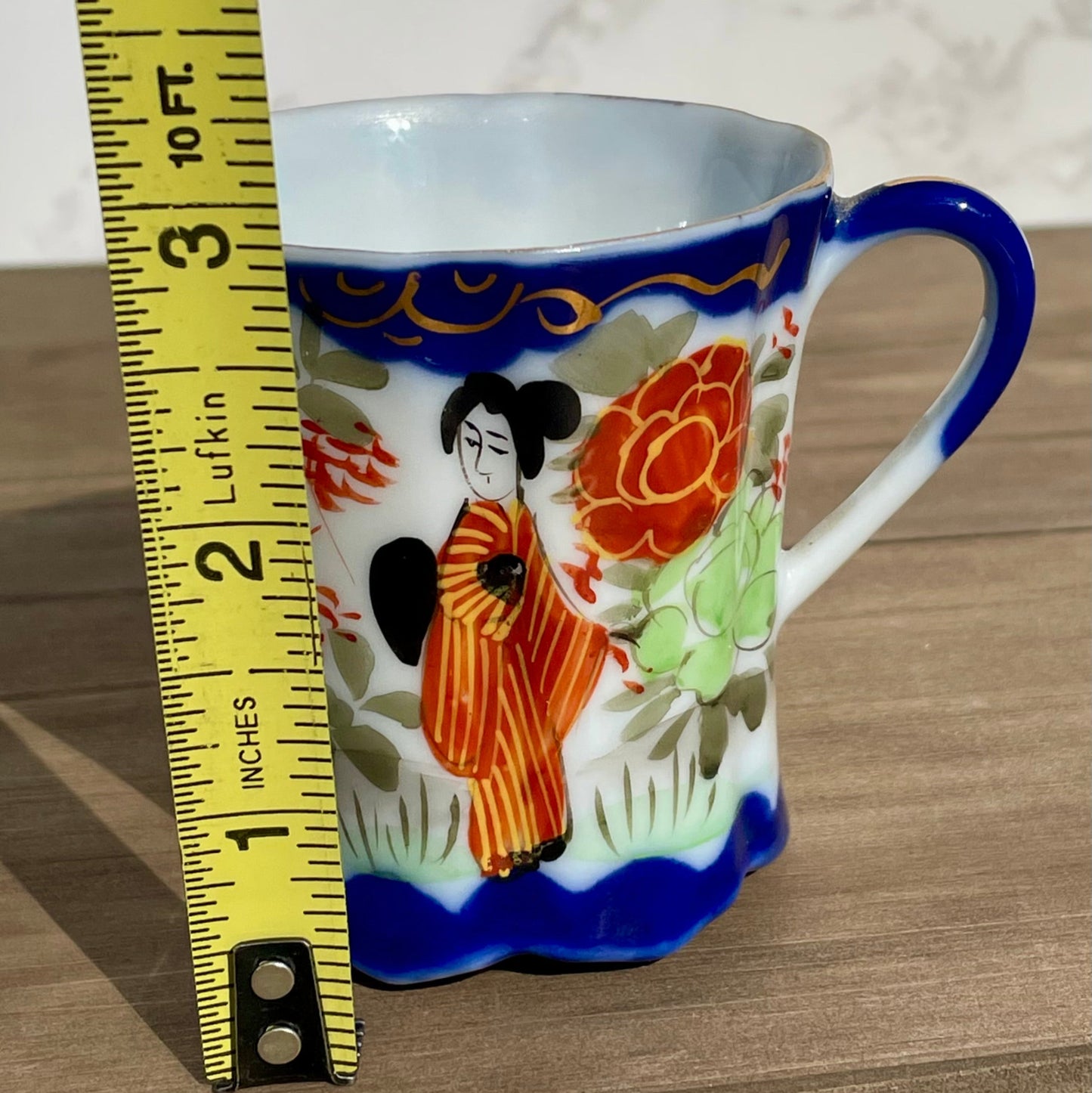 vintage sake tea cup with geisha and flowers hand painted japanese blue rimmed scalloped edge cup made in japan tall and selnder cup geisha girl in red dress red flowers gold embellishments green plants japanese landscape hand painted image scalloped base tea cup sake cup vintage gift asain inspired asain kitchen asain cup asain home decor thebrokenbirdcompany free shipping