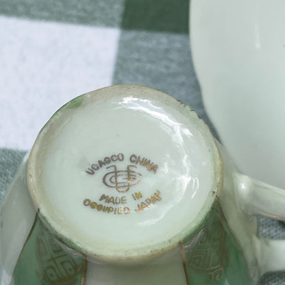 Close-up of a ceramic product with a visible brand logo on a checkered fabric background UCAGCO green and gold tea cup and saucer plate the broken bird company free shipping gift tea set
