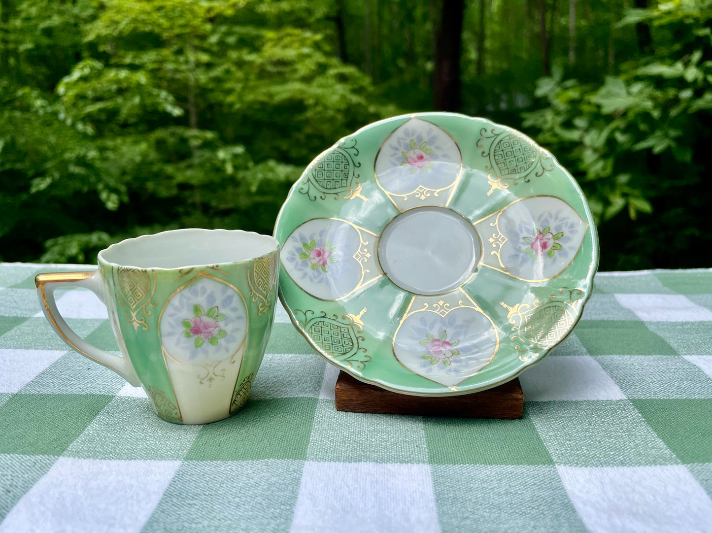 Green ceramic teacup and saucer with floral patterns on a checkered tablecloth.