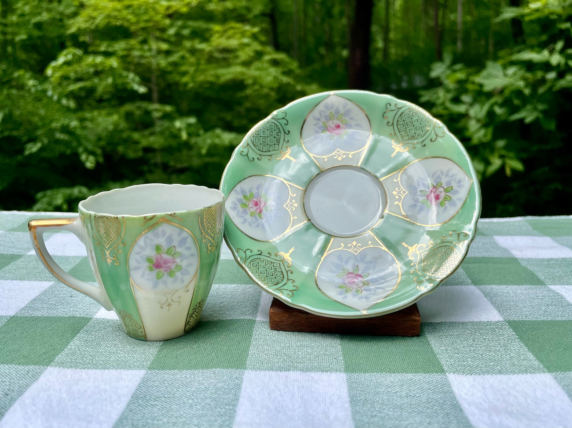 Green ceramic teacup and saucer with floral patterns on a checkered tablecloth.