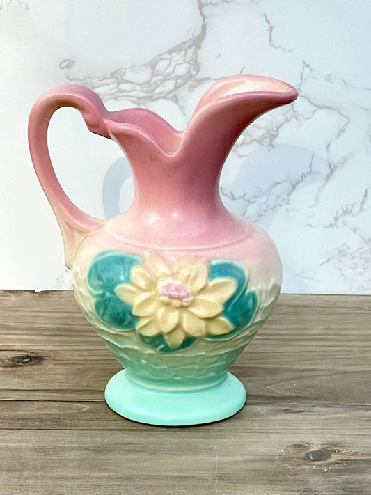 A vintage Hull Art ceramic pitcher with a Magnolia design featuring teal and pink hues. The pitcher has a handle on the left, a spout on the right, and sits on a flat base.