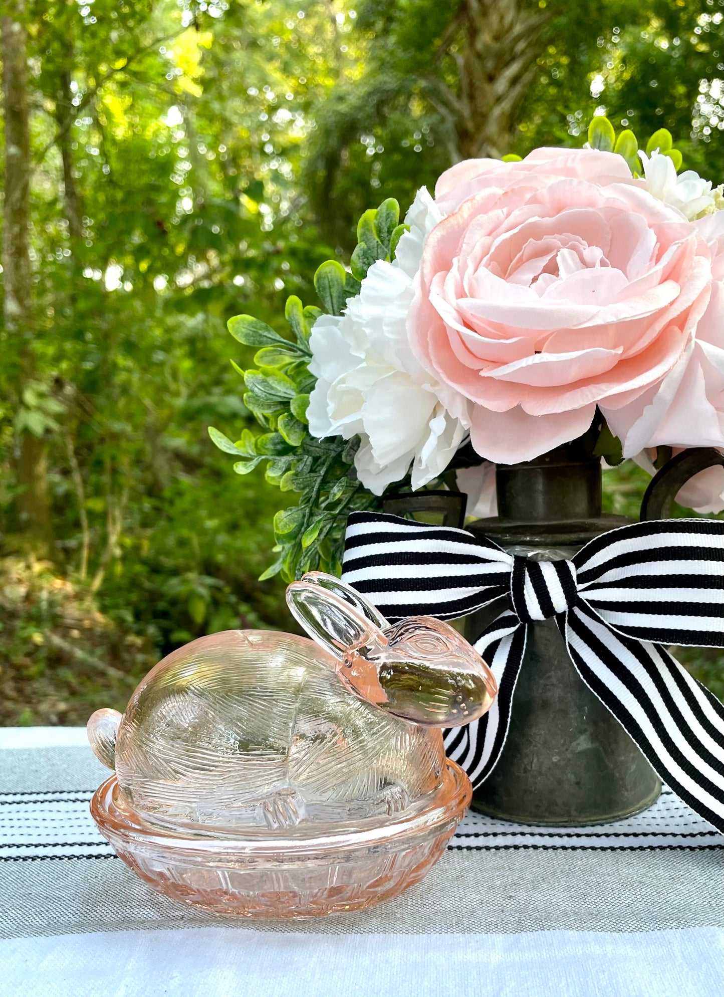 A pink glass figurine of a bunny sitting on a basket, used as a covered dish.