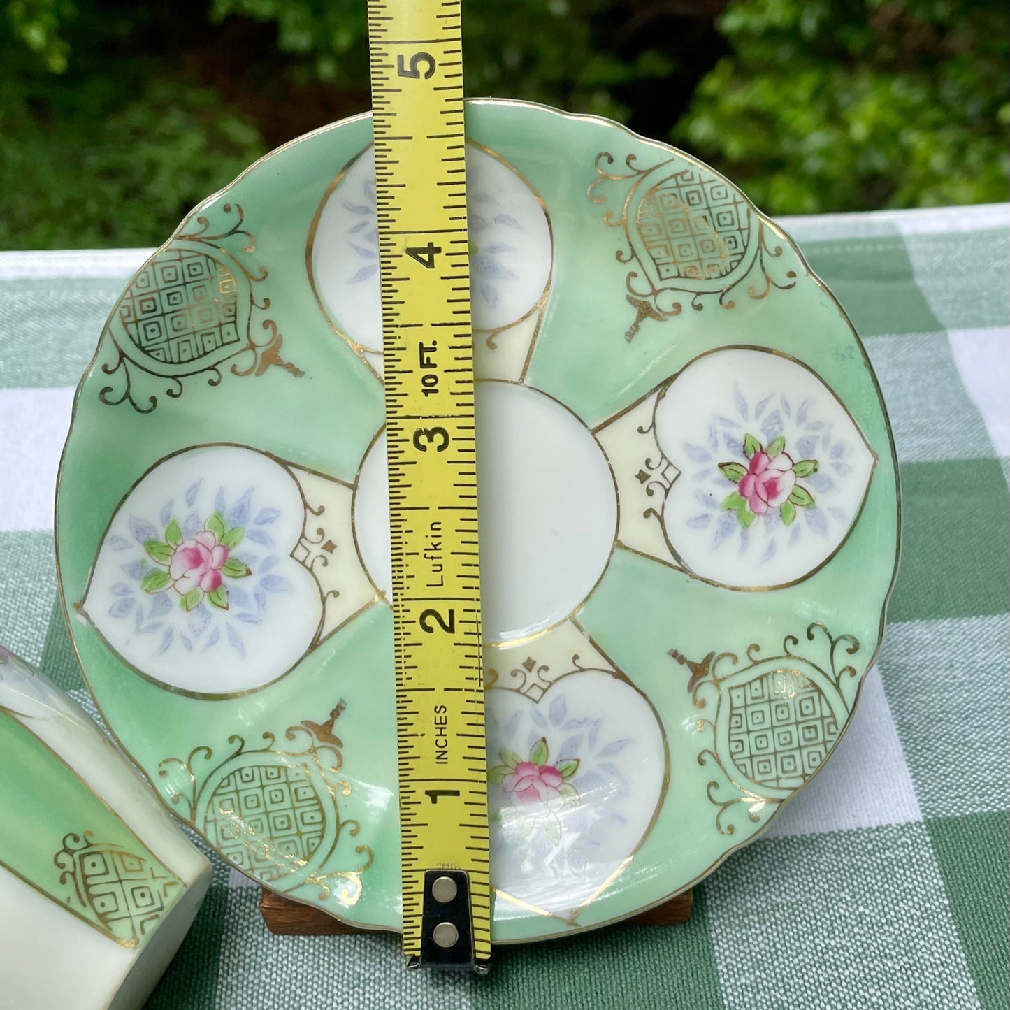 Decorative ceramic plate with floral patterns and a measuring tape for scale on a green checkered tablecloth.